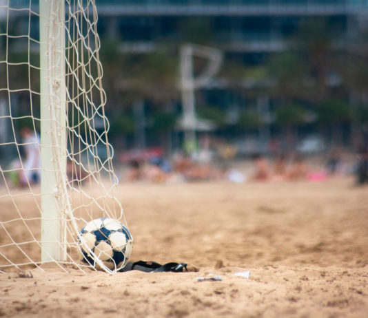 Un balón descansa dentro de las redes de un campo de fútbol playa.