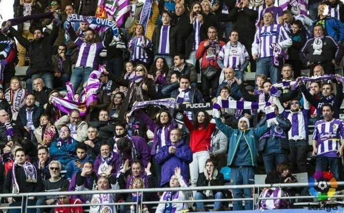 En la imagen se ve la grada del estadio Carlos Tartiere con varios aficionados del Real Valladolid portando banderas de hermanamiento con el Real Oviedo
