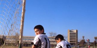Dos niños uniformados esperan el inicio de un partido junto a la portería de un campo de fútbol de albero. Rodrigo Ferrari